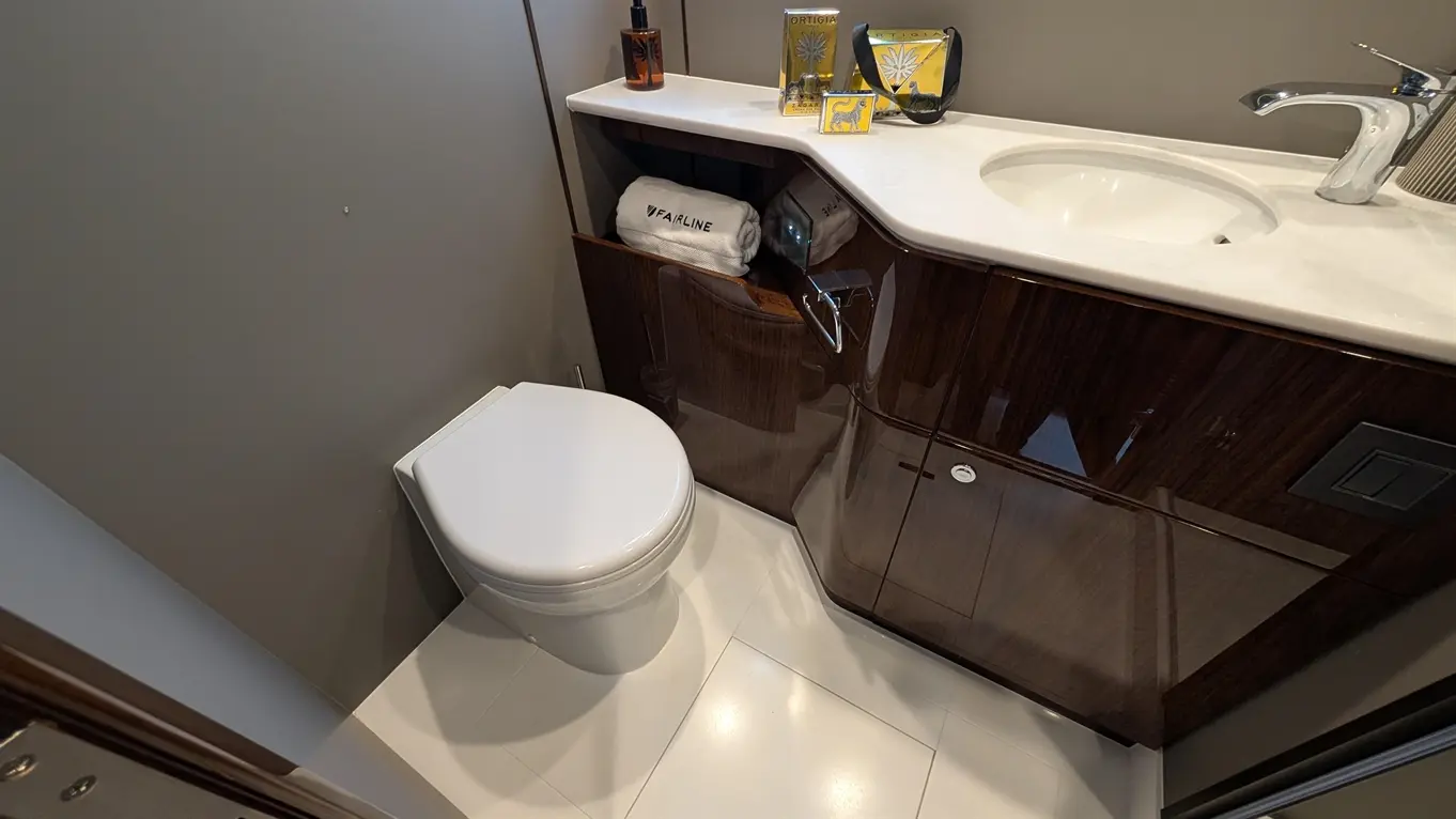 Modern bathroom featuring a white toilet, vanity with marble top, towels, and luxury toiletries on display.